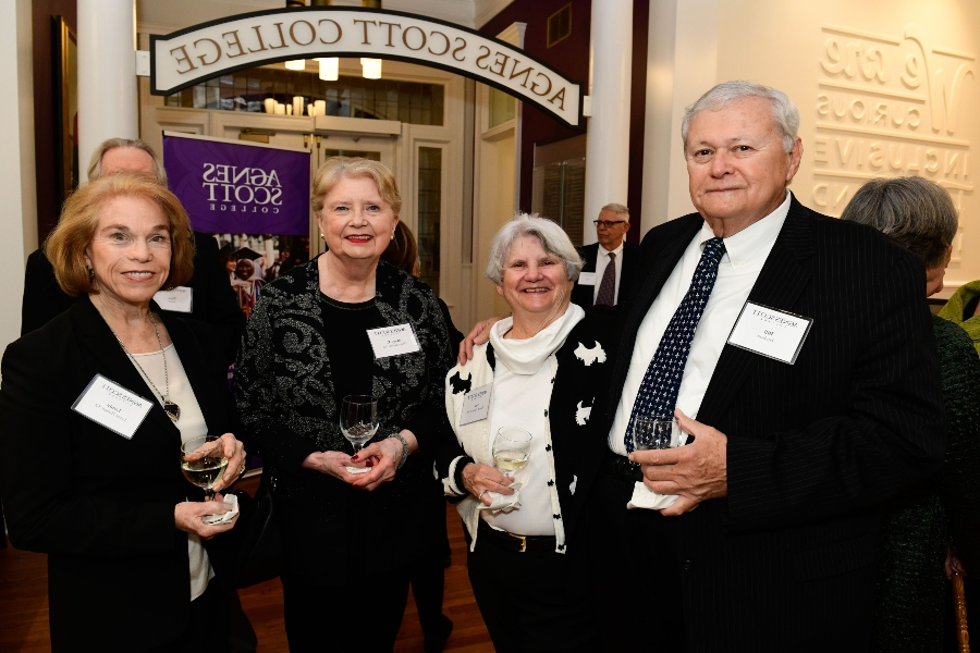 A group of donors stand together in a row with an artistic arch in the background that reads Agnes Scott College